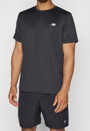 Uomo che indossa una maglietta sportiva nera a maniche corte e pantaloncini abbinati con logo New Balance bianco su sfondo neutro.