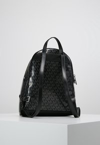 Zaino nero in pelle lucida, caratterizzato da un motivo a logo ripetuto, doppie spalline e una tasca laterale con zip.