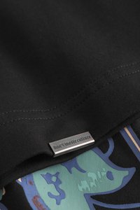 Black cotton fabric with a smooth texture features a sewn label reading "don't waste culture," overlaying a patterned blue and green design.