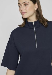 Top atlético azul marino con cuello alto, cremallera frontal, mangas cortas y textura suave. Diseño simple y moderno.