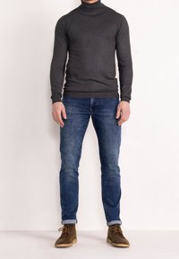 Pull à col roulé gris, manches longues, coupe slim ; assorti à un jean slim bleu ; bottines en daim marron avec lacets et revers retroussés.