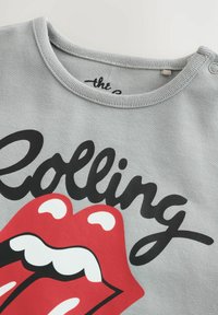 Sweat-shirt gris avec du texte en noir "Rolling" et un grand graphique de langue rouge, accompagné d'accents blancs et d'un design de col rond.