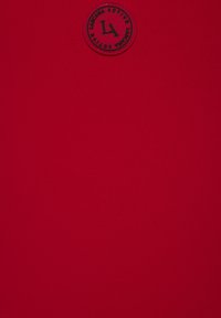 Roter Stoff mit glatter Textur, der ein rundes schwarzes Logo mit "LA" und Markeninformationen zeigt. Schlichter Hintergrund ohne zusätzliche Elemente.