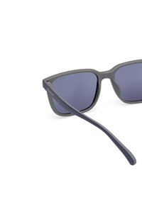 Ochelari de soare gri din plastic cu un cadru flexibil, lentile de culoare albastru închis și un braț subțire cu numele mărcii "GANT" embossat.