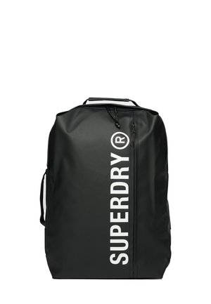 Mochila impermeable negra con logo blanco "SUPERDRY", cierre con cremallera y asas laterales. Presenta un diseño rectangular limpio con correas ajustables.