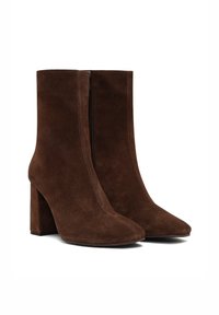 Botas de tobillo de ante marrón con punta afilada, textura suave y cremallera lateral. El grueso tacón bloque agrega estabilidad al diseño.