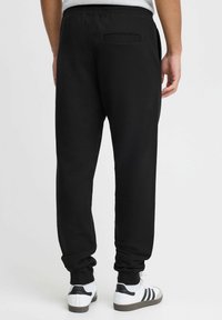 Svarte joggebukser med elastisk midje, sidelommer og en enkel baklomme. Materialet ser mykt ut med en jevn tekstur. Bukseben med mansjetter.