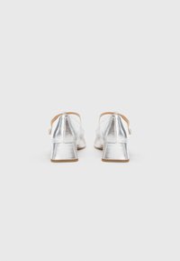 Silver metallic block-heeled shoes with a smooth texture, open back design, and a small strap across the ankle.