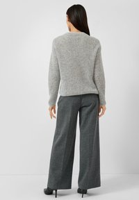 Hellgrauer, gerippter Pullover mit rundem Ausschnitt, kombiniert mit dunkelgrauen, weit geschnittenen Hosen. Glatte Textur und lockere Passform.