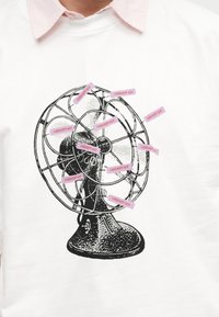 Μαύρο vintage γραφικό ανεμιστήρα σε λευκό ύφασμα με πολλαπλές ροζ αυτοκόλλητες ετικέτες με την επιγραφή "CARHARTT WIP" στα πτερύγια και το πλέγμα του ανεμιστήρα.