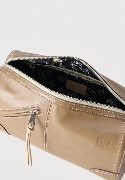Μπεζ δερμάτινη τσάντα καλλυντικών με ασημένια φερμουάρ, μπροστινή τσέπη και μαύρη εσωτερική επένδυση με λευκά αφηρημένα σχέδια.