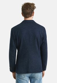 Marineblaues, strukturiertes Blazer mit Reverskragen, seitlichem Schlitz und geknöpften Manschetten, kombiniert mit hellblauen Jeans.