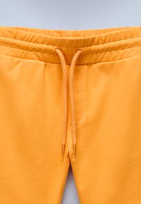 Oranga sweatpants med elastisk midja och dragsko samt en slät, mjuk textur. Tyget är lätt och bekvämt.