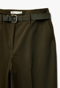 Olivevihreät räätälöidyt housut, joissa on suora pinta, varustettuna yhteensopivalla vyöllä, jossa on hopeinen solki ja etutaskut.