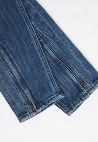 Tmavě modré džíny z denimu mají zipové uzávěry na manžetách a texturední povrch s viditelným šitím a detaily blednutí.