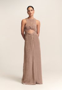 Długa, bezrękawnikowa sukienka z miękkiej, jasnobrązowej tkaniny. Posiada skręcony wycięcie w talii oraz zwiewną spódnicę. Gładka faktura, elegancki design.