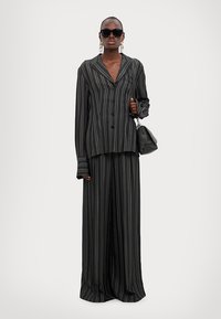 Black and gray pinstripe oversized suit set with long sleeves, wide-leg trousers, paired with black sunglasses and a small green bag.