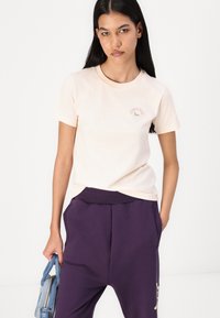 Ljusrosa bomulls t-shirt med korta ärmar, som har en liten grön och röd "Converse" logotyp på bröstet. I kombination med lila sweatpants.