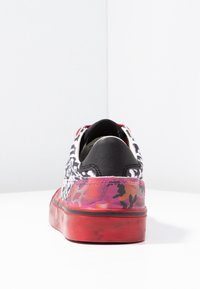 Baskets avec un dessus à motifs noir et blanc, semelle rouge, et accents camouflés multicolores. Forme arrondie avec un design bas.