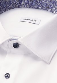 Wit overhemd met zwarte knopen, voorzien van een col met paisleypatroon en een label van het merk "Seidensticker".