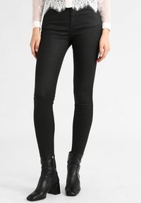 Jeans negros ajustados de tela elástica, con un acabado suave y un diseño ceñido, combinados con botas negras de tobillo con un tacón grueso.