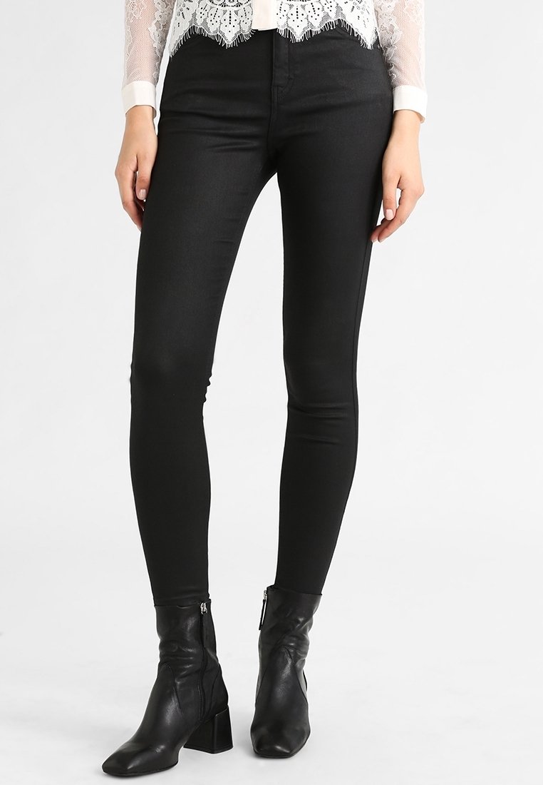 Jeans negros ajustados de tela elástica, con un acabado suave y un diseño ceñido, combinados con botas negras de tobillo con un tacón grueso.
