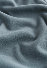 Tissu doux et texturé dans une couleur bleu-gris doux, présentant de douces vagues et plis, avec des variations de surface lisses et de la profondeur.