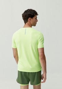 Kortärmad atletisk skjorta i klargul limegrön, med rund halsringning och ett grått vertikalt streck på baksidan. Slät textur.