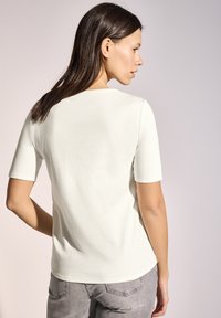 T-shirt à manches courtes de couleur crème en coton, avec un col rond et des lignes épurées, présentant une texture douce et une coupe décontractée.
