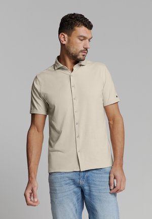Korte mouwen beige shirt met een kraag, voorzien van een knoopsluiting aan de voorkant en een kleine knoopaccent op de mouw. Gladde textuur van de stof.