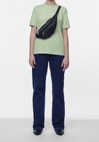T-shirt verde, jeans in denim blu scuro e una borsa a tracolla in pelle nera con doppia cerniera. Design semplice con vestibilità rilassata.