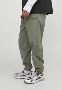 Pantalones de tiro ajustado en color verde claro, con cintura elástica, bolsillos laterales y el nombre de la marca "JACK & JONES" impreso en negro. Llevados con zapatillas deportivas.