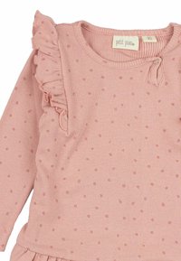 Top rosa a coste con maniche lunghe, caratterizzato da dettagli arricciati, piccoli pois e una chiusura con bottone al collo. La texture è morbida ed elastica.