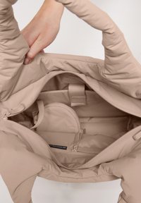 Borsa tote di un leggero beige con una texture trapuntata, dotata di chiusura con zip e scomparti interni per l'organizzazione. Le maniglie sono morbide e resistenti.