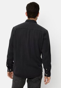 Chemise noire en coton à manches longues avec un col classique, des poignets boutonnés et un ourlet droit. Texture lisse et design minimaliste.
