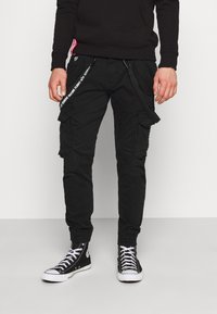 Svarta cargobyxor med flera fickor och justerbara remmar. Har en mjuk textur och smal passform, i kombination med svarta högskurna sneakers.