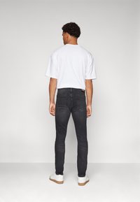 Fekete slim fit farmernadrág, öt zsebbel, fehér, rövidujjú pólóval és fehér sportcipővel párosítva. Sima textúra, modern szabás.