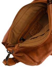 Braune Lederhandtasche mit einem Reißverschluss oben, die ein geräumiges Innenleben mit beigem Stofffutter bietet, einschließlich einer Innentasche und einem Markenlabel.