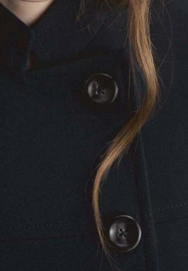 Navy wool coat with a high collar, featuring two large black buttons and stitching detail. A strand of hair rests against the fabric.