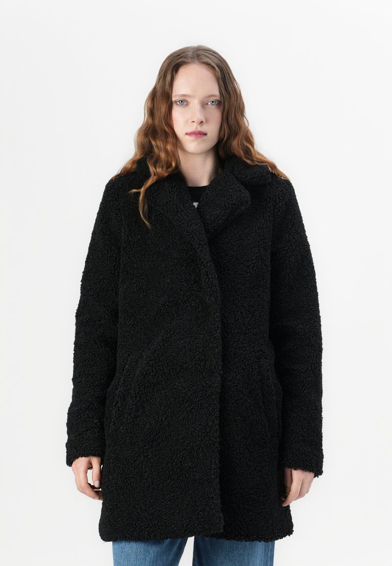 Black, textured, oversized coat with a collar, long sleeves, side pockets, and a soft, fleece-like exterior.