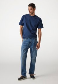 Navy cotton t-shirt with short sleeves, paired with light blue denim jeans and dark shoes featuring brown laces and a white sole.
