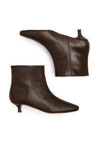 Botas de cuero marrón hasta el tobillo con punta afilada, superficie texturizada, tacón kitten bajo y un diseño único en la parte trasera alta.