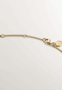 Pulsera de cadena de oro con eslabones redondos entrelazados, con un cierre de langosta y un charm circular grabado. Superficie lisa y brillo metálico.