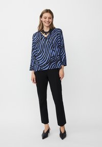 Blauw en zwart gestreepte blouse met een V-hals, lange mouwen en twee knopen. Gepaard met zwarte op maat gemaakte broeken en puntige schoenen.