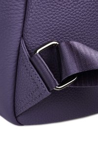 Coin du sac en cuir texturé violet avec des bords cousus, arborant un anneau en D métallique et une sangle en satin repliée.