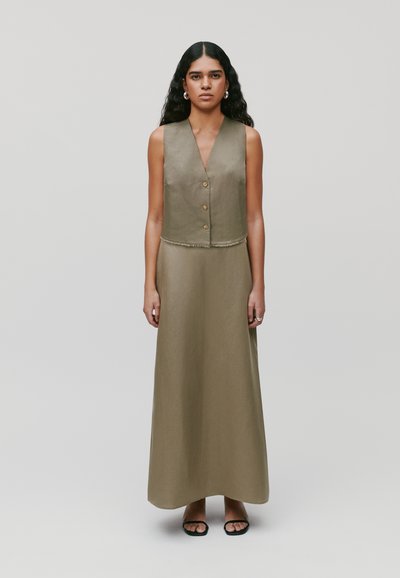 Gilet in lino verde oliva e abito maxi, con scollatura a V profonda, tre bottoni, bordi sfrangiati e una texture liscia, abbinato a sandali neri.