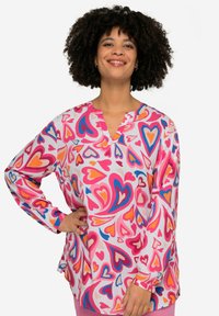Farverig bluse med lange ærmer, der har en hvid baggrund med forskellige hjerte-mønstre i pink, blå og orange. V-hals design og afslappet pasform.