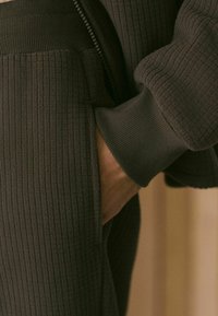 Tamno sivi rebrasti džemper sa patentnim zatvaračem, sa teksturiranim materijalom i bočnim džepom. Manžetna je glatka i rebrasta.