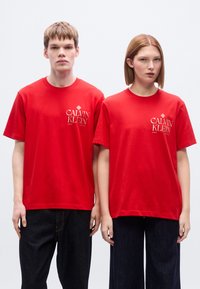 Κόκκινα βαμβακερά t-shirt με κοντά μανίκια, με το λευκό λογότυπο «CALVIN KLEIN» στο αριστερό στήθος. Συνδυάζονται με σκούρα μπλε τζιν.