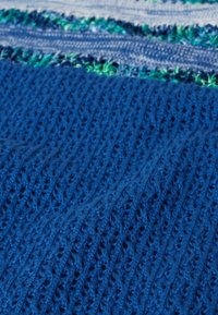 Gestrickter blauer Stoff mit einer strukturierten, gerippten Musterung und kleinen Öffnungen, ergänzt durch horizontale Streifen in Grün und Hellblau.